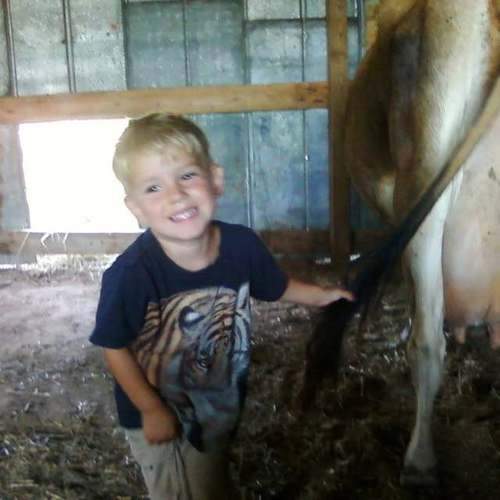 Judah Leathers grinning while helping with milking chores at C4 Farms El Dorado Springs